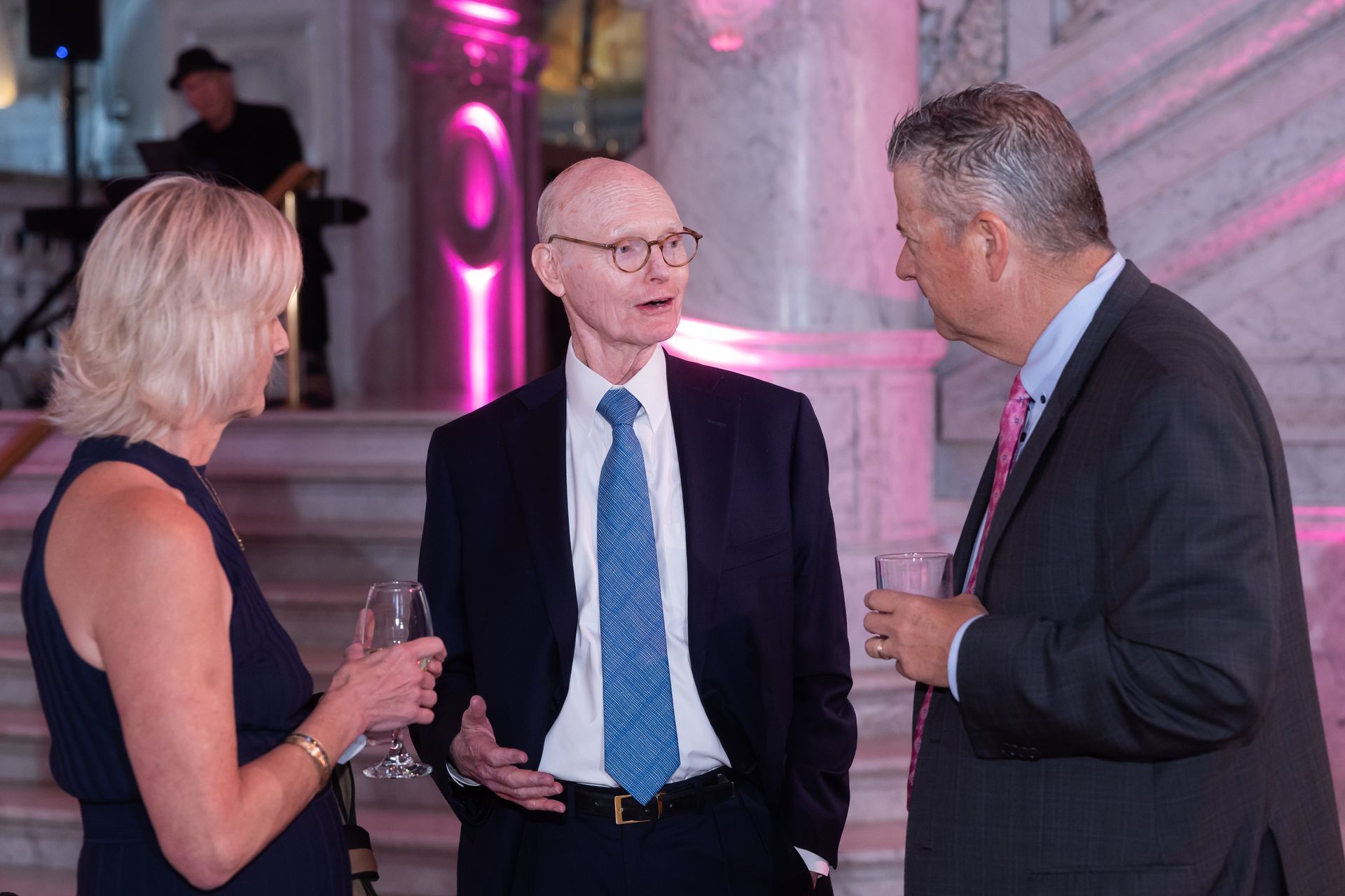 A man in a suit and tie is talking to two other men and a woman.