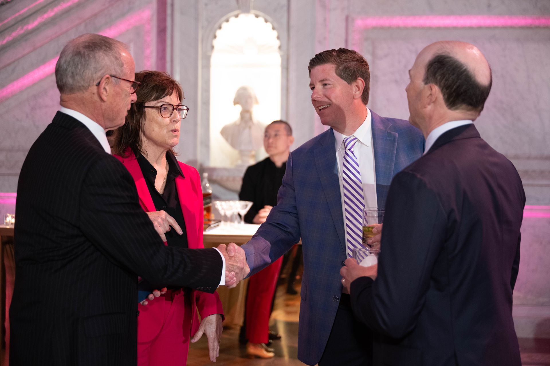 A group of people in suits are shaking hands in a room.