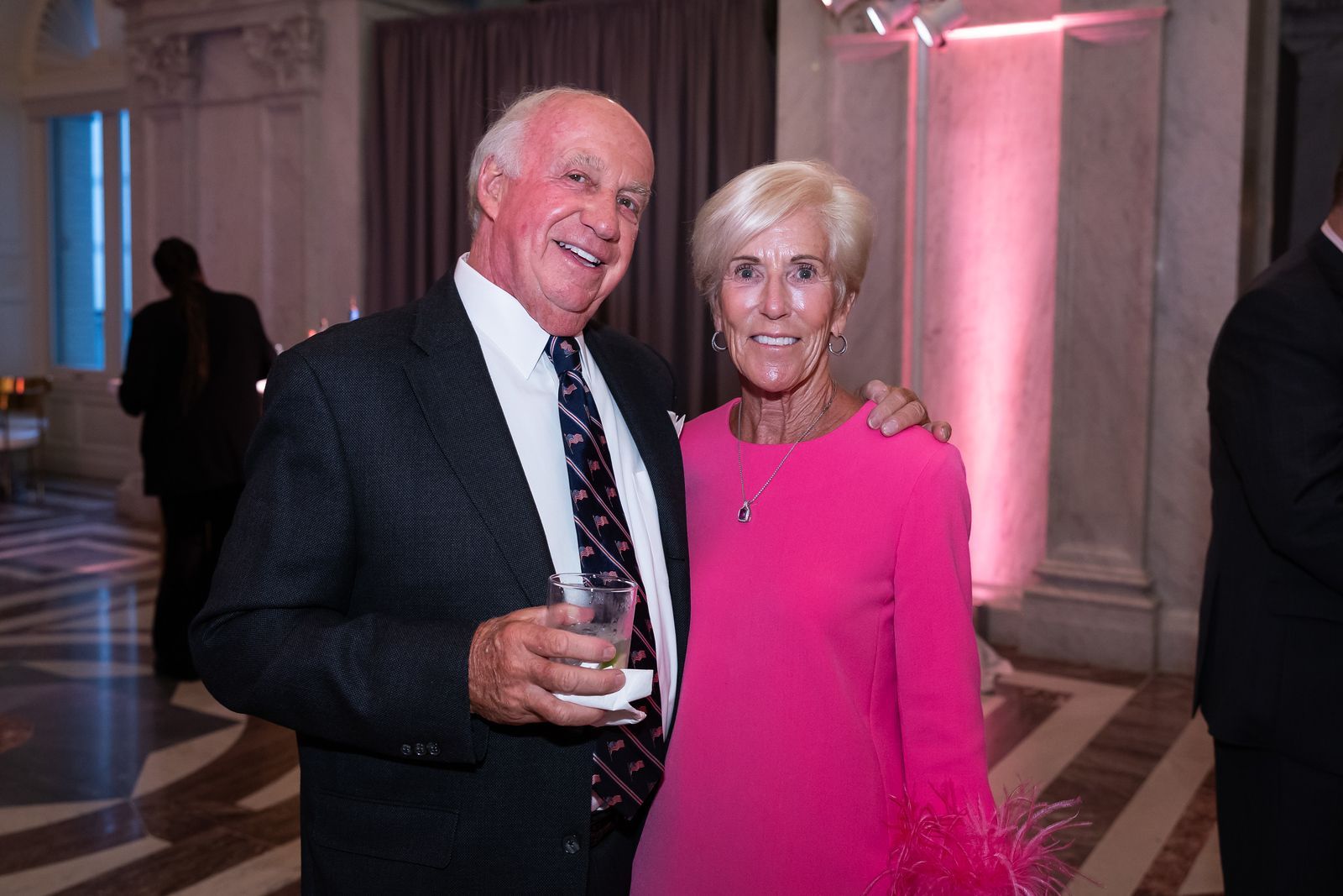 A man and a woman are posing for a picture at a party . the woman is wearing a pink dress.