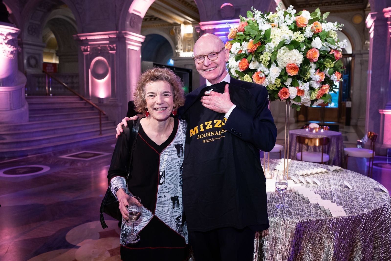 A man and a woman are posing for a picture in a room with flowers in the background.