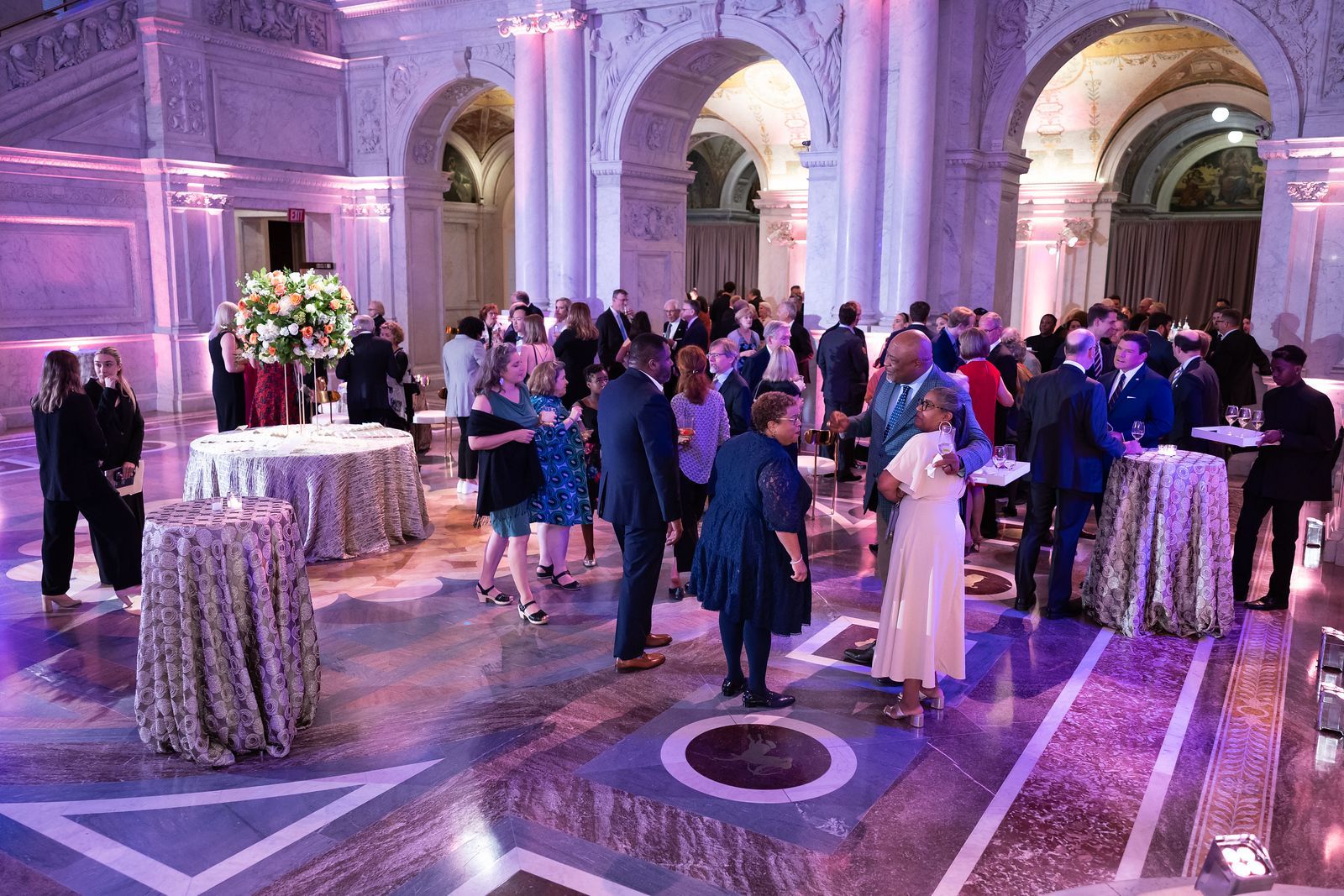 A large group of people are standing around tables in a large room.