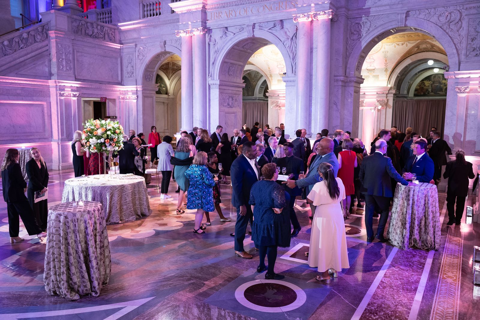 A large group of people are standing around tables in a large room.