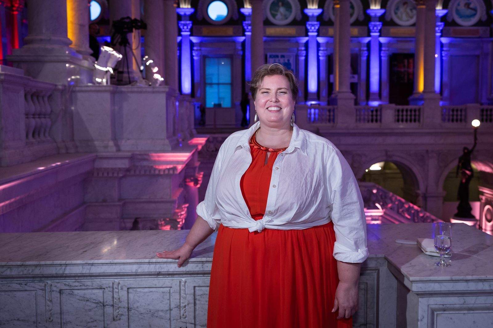A woman in a red dress and white shirt is standing in front of a building.