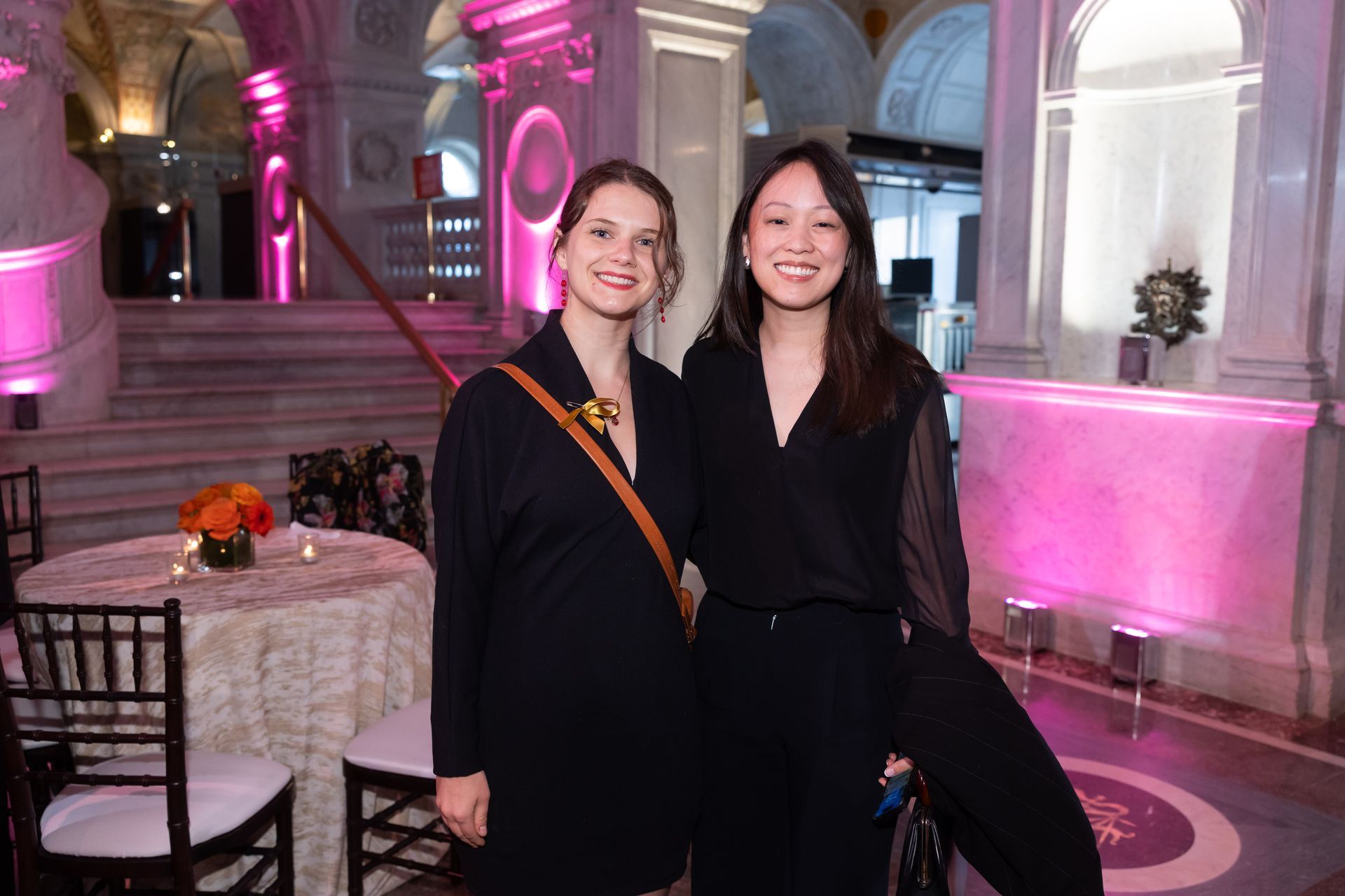 Two women are posing for a picture in a room with pink lights.