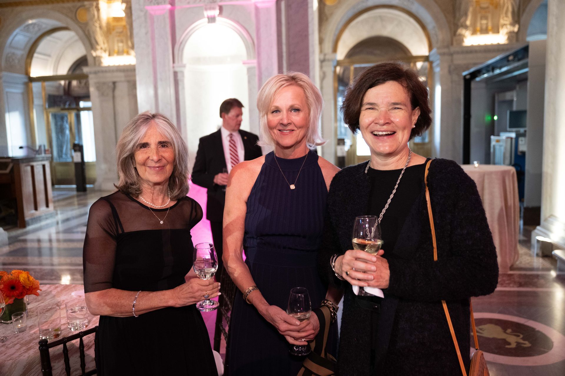 Three women are standing next to each other in a room holding wine glasses.