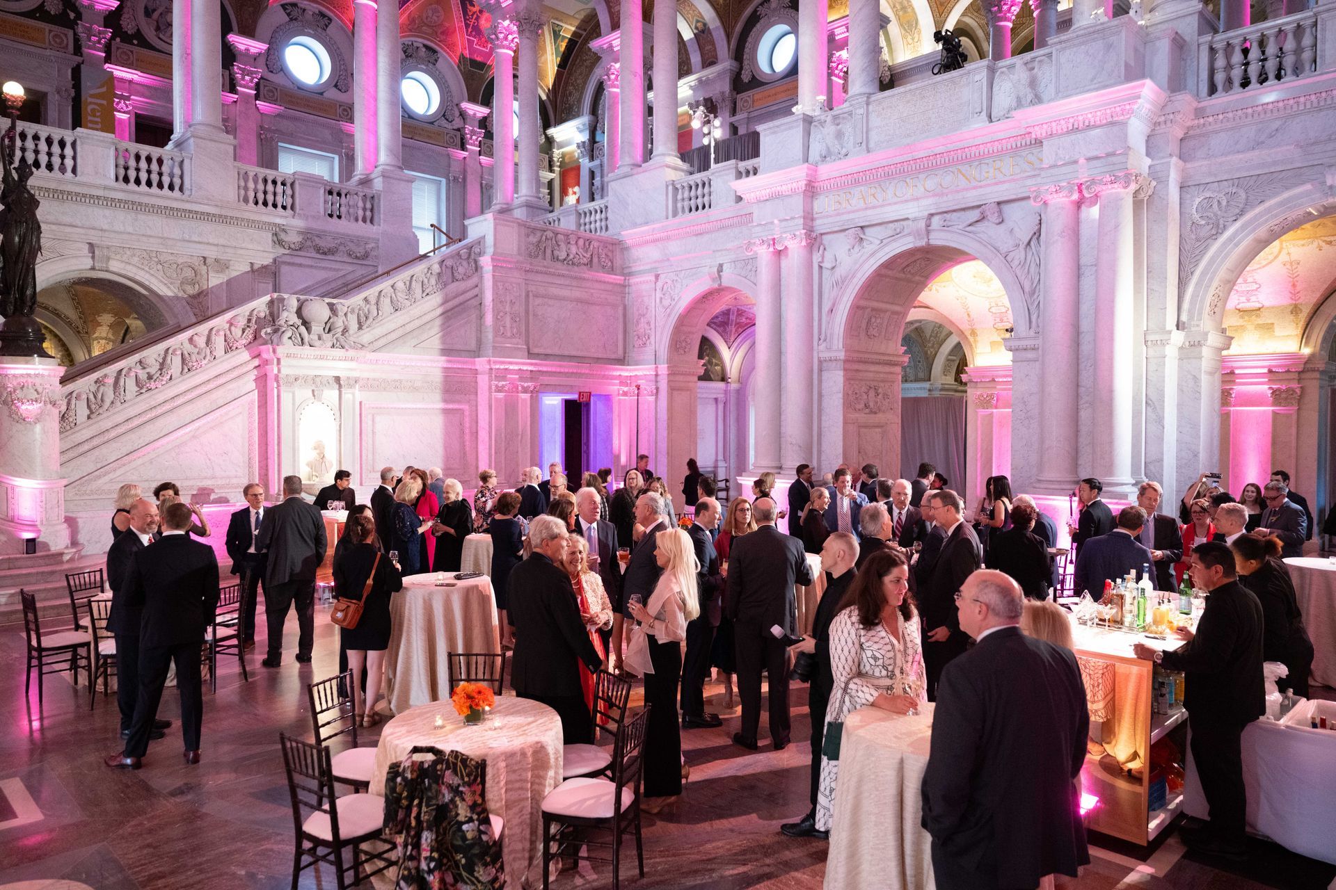 A large room filled with people standing around tables and chairs.