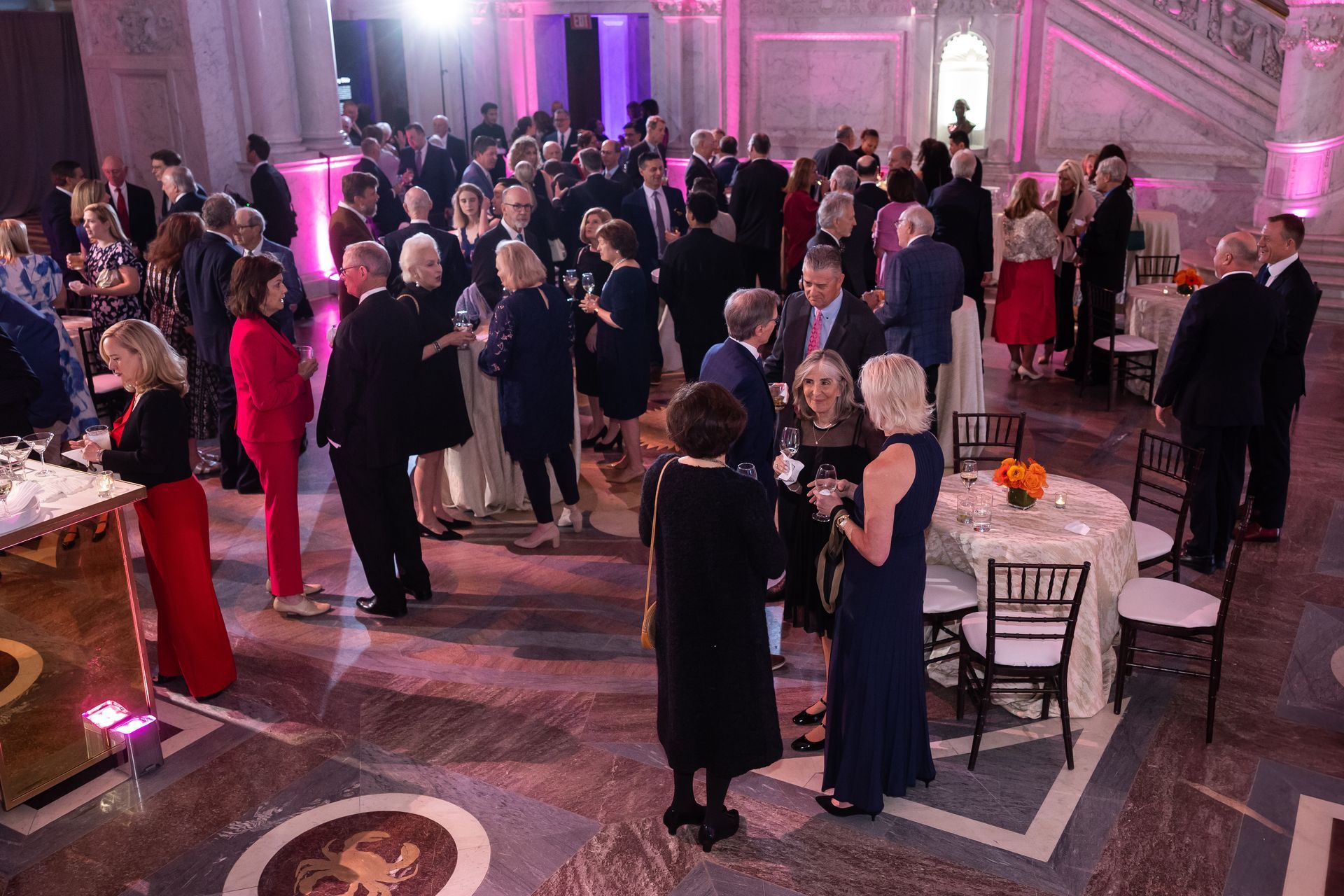 A large group of people are standing around tables and chairs in a large room.