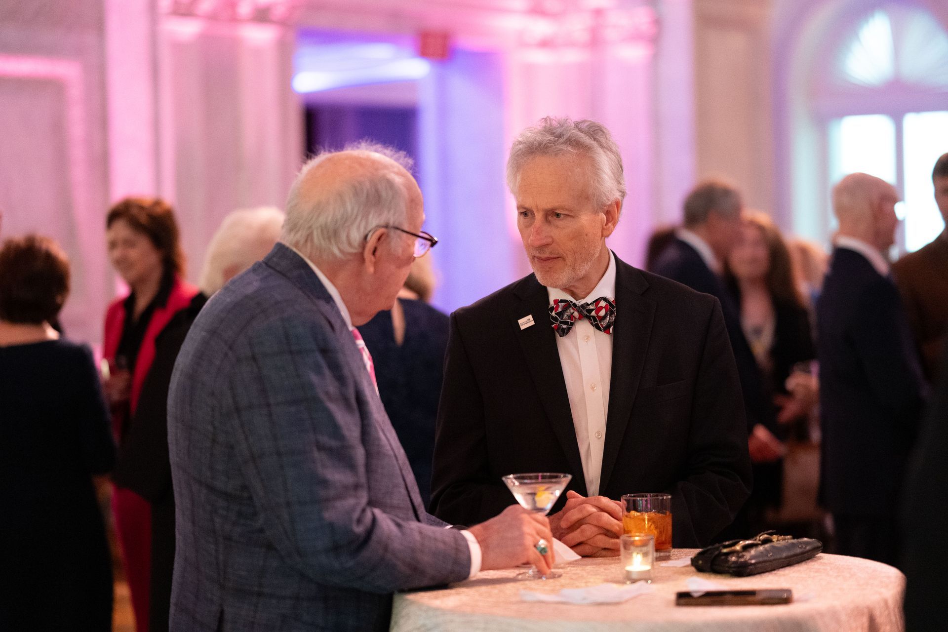 Two men are sitting at a table talking to each other at a party.