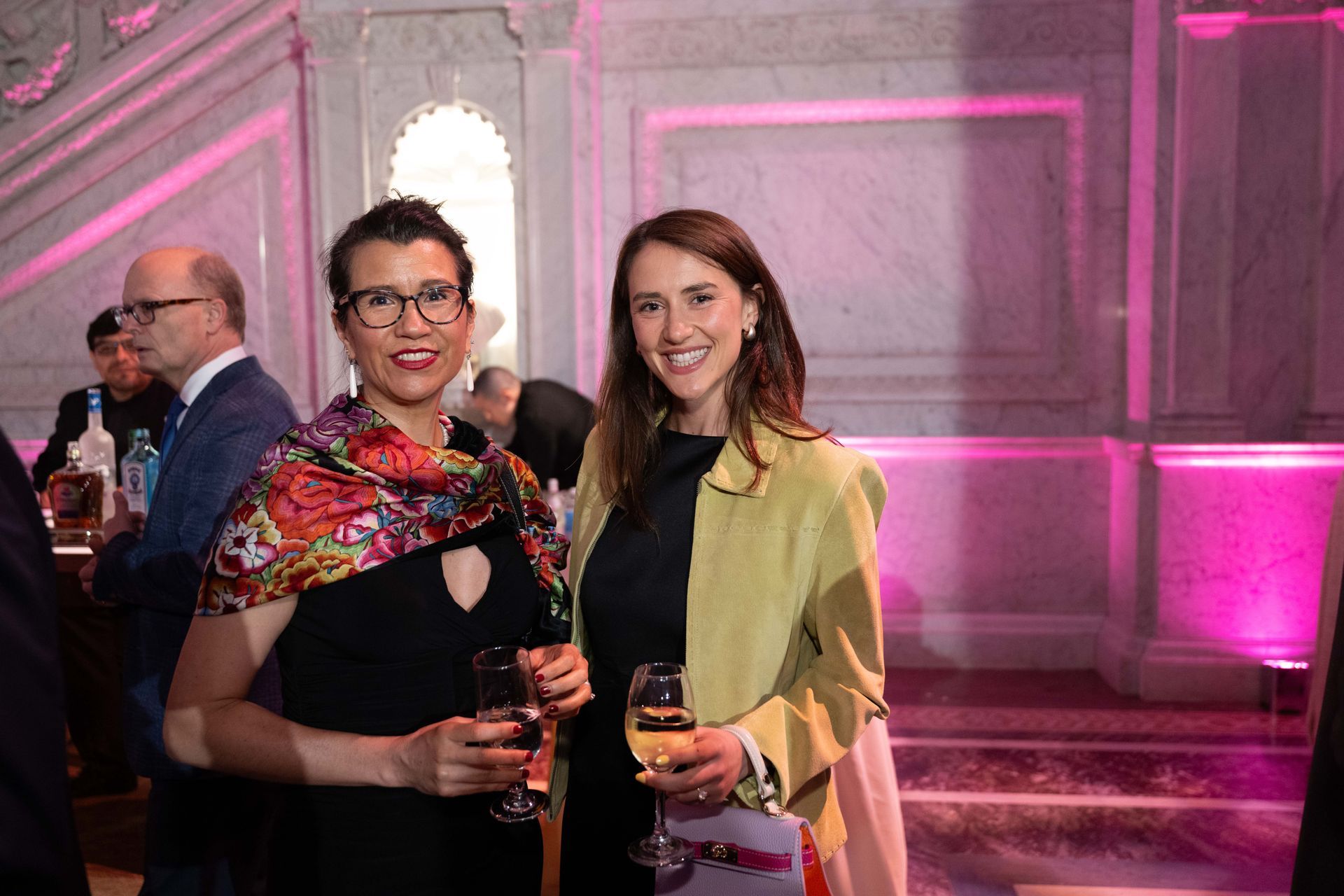 Two women are standing next to each other in a room holding wine glasses.