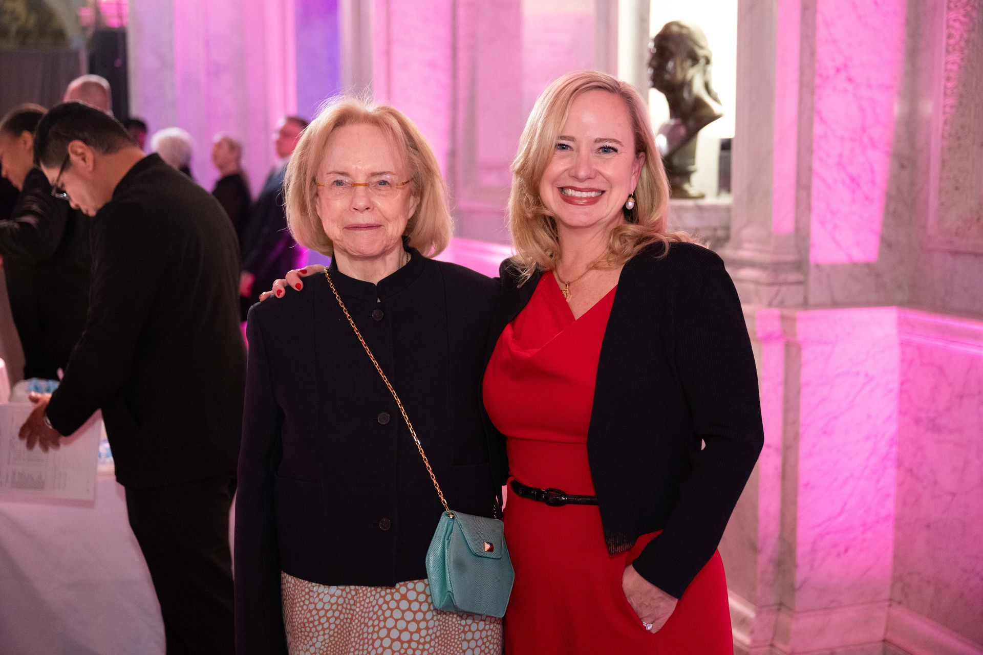 Two women are posing for a picture in a room with pink lights.