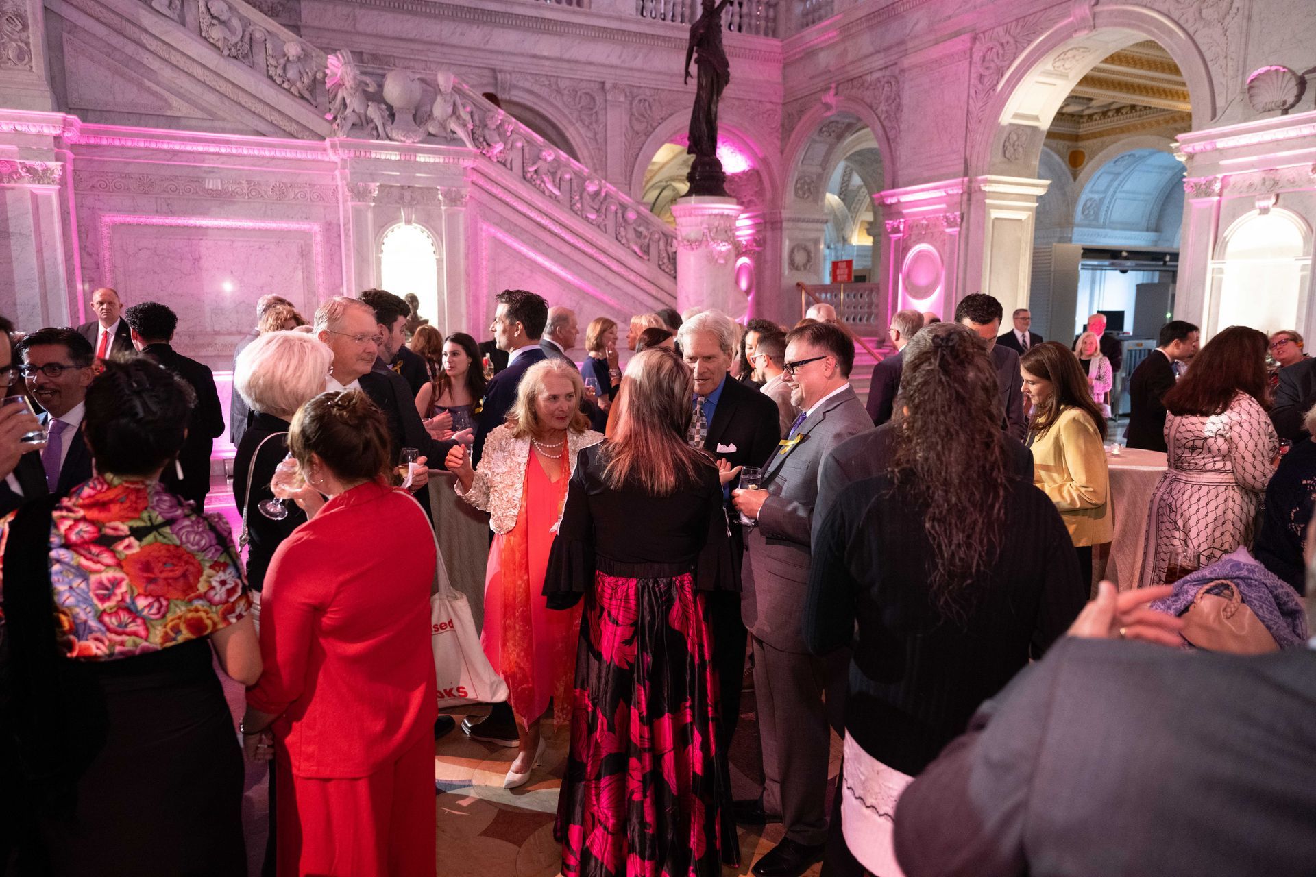 A large group of people are standing in a room with pink lights.