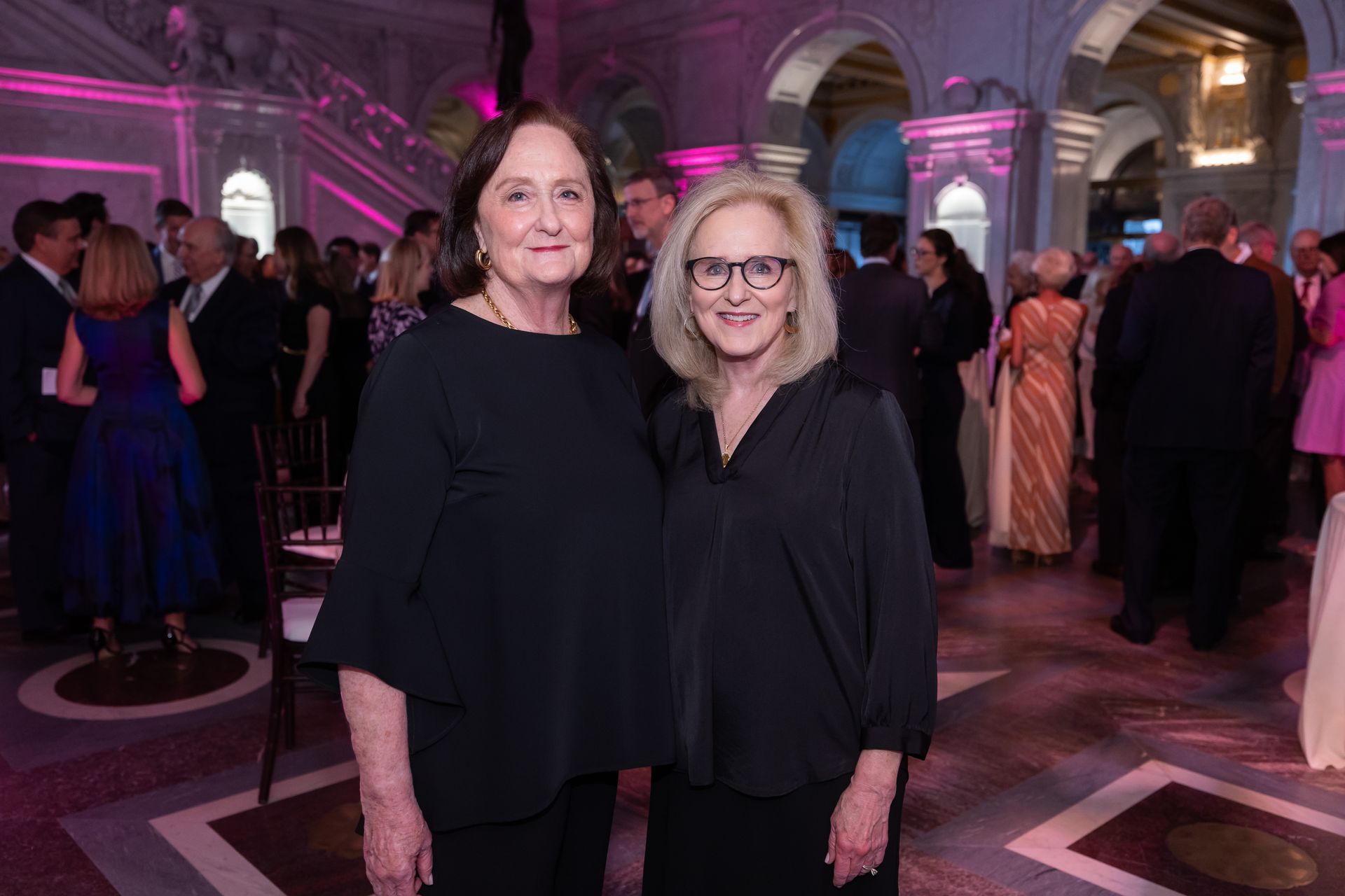 Two women are standing next to each other in a room at a party.
