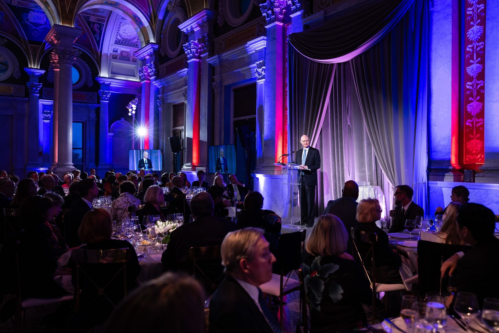 A man is giving a speech in front of a crowd at a banquet.