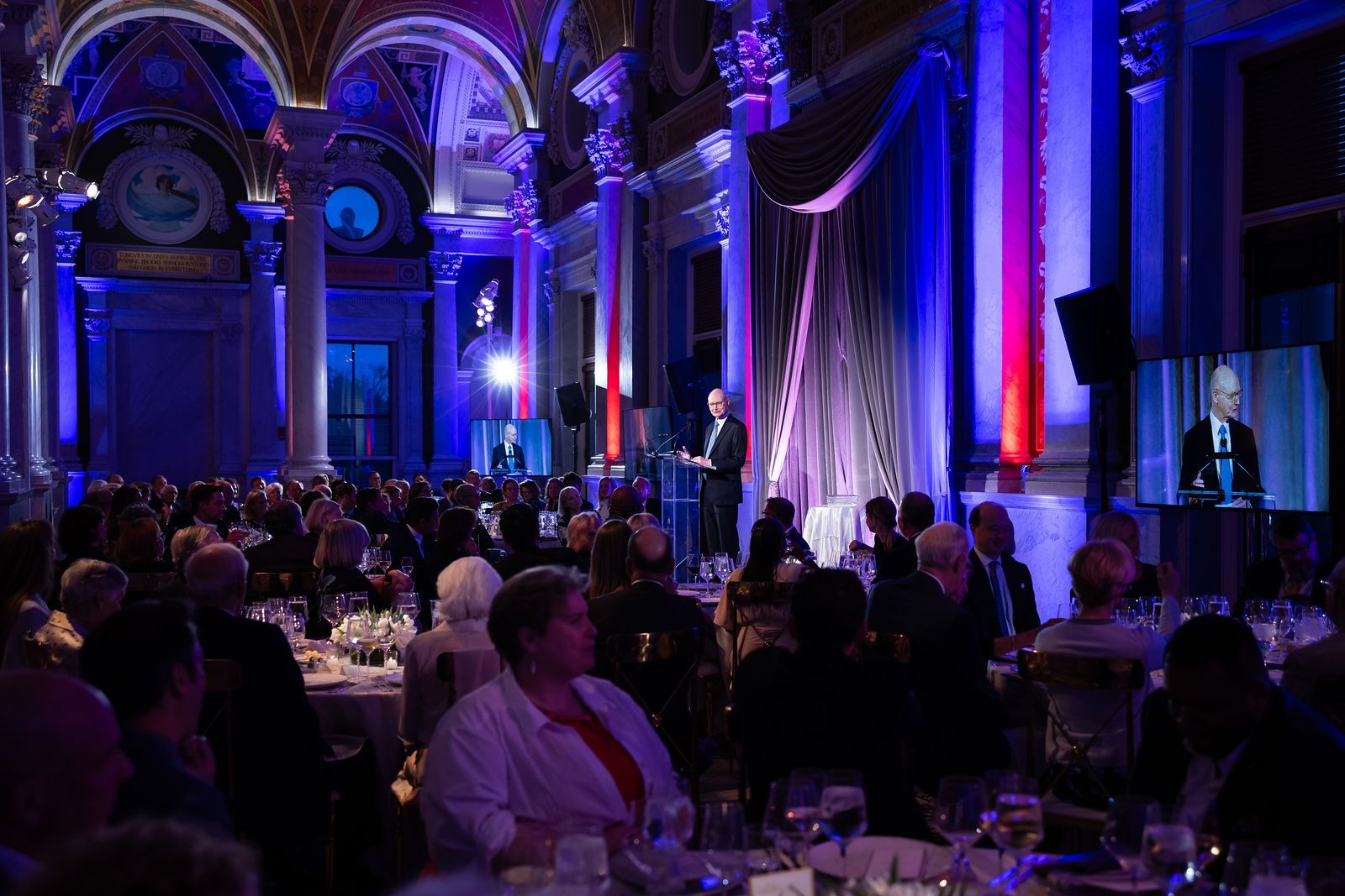 A man is giving a speech at a banquet in a large room.