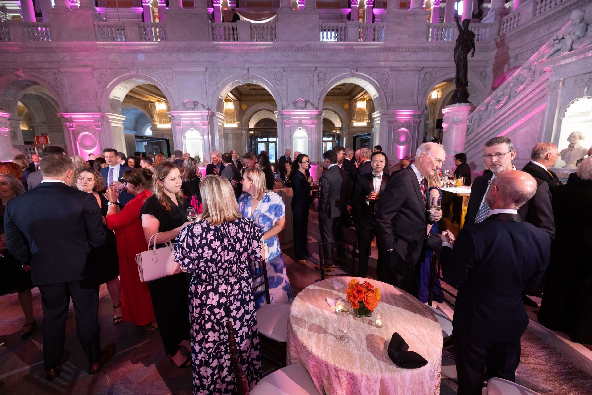 A large group of people are standing around tables in a large room.
