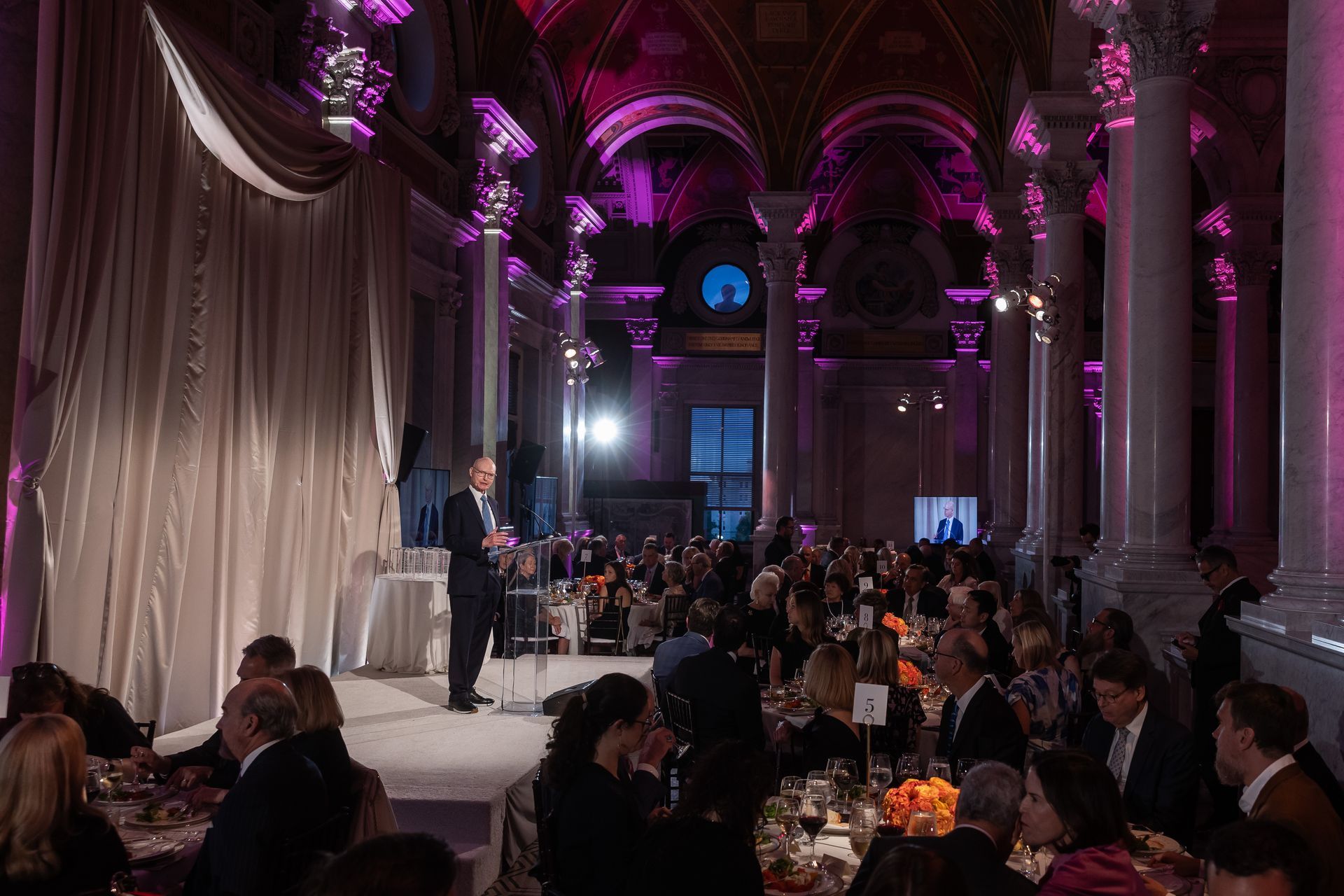 A man is standing on a stage in front of a crowd of people at a banquet.