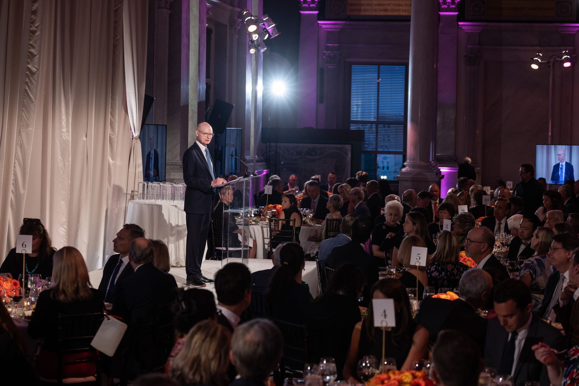 A man is giving a speech at a podium in front of a crowd of people.