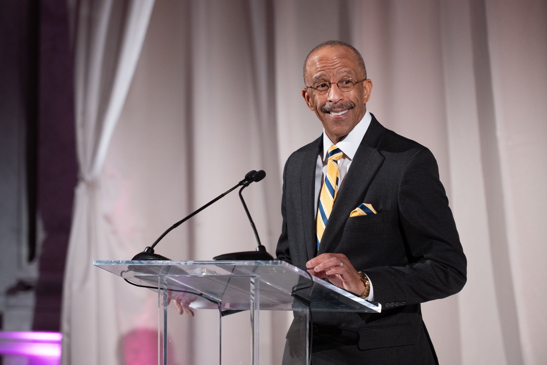 A man in a suit and tie is giving a speech at a podium