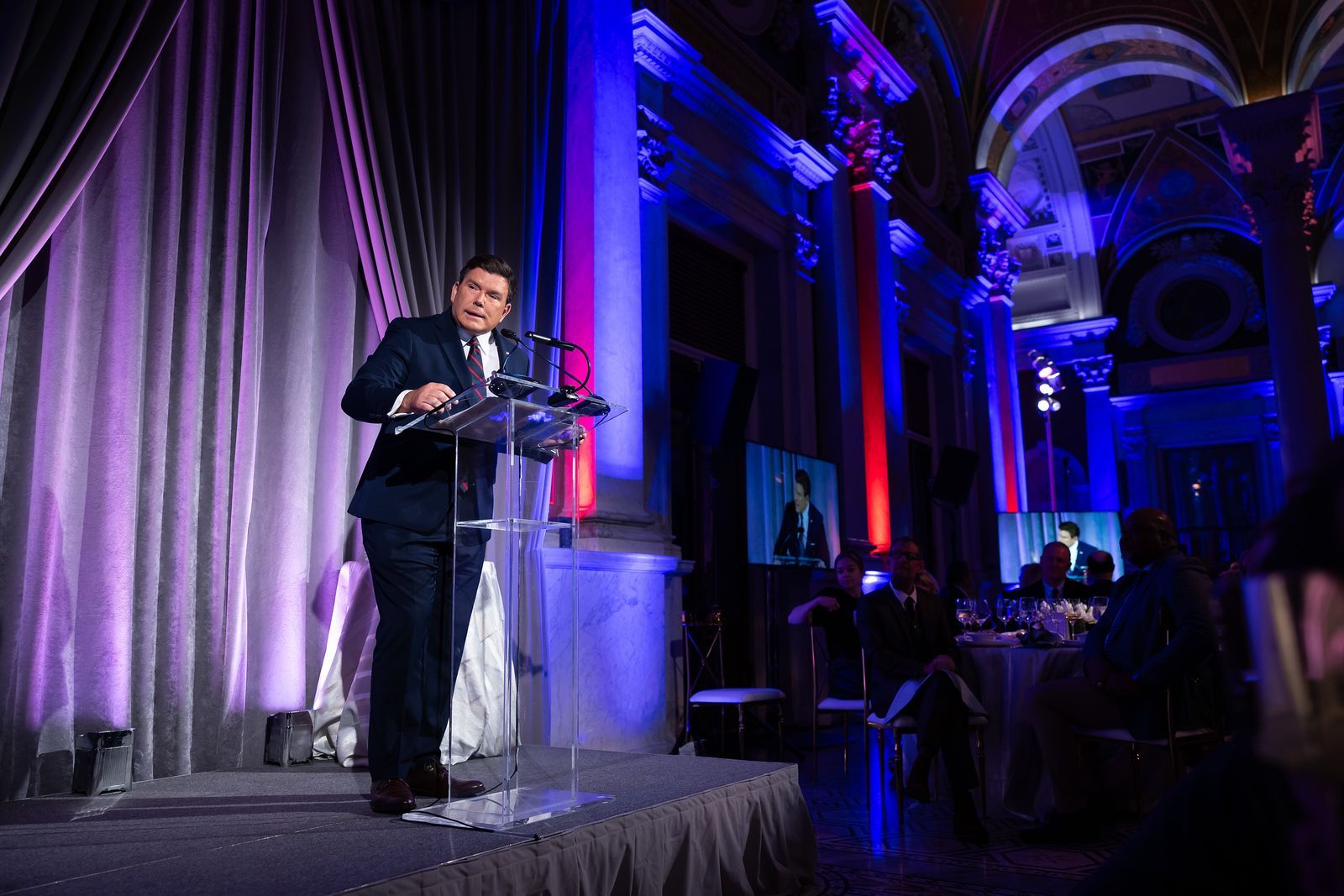 A man in a suit is standing at a podium giving a speech.