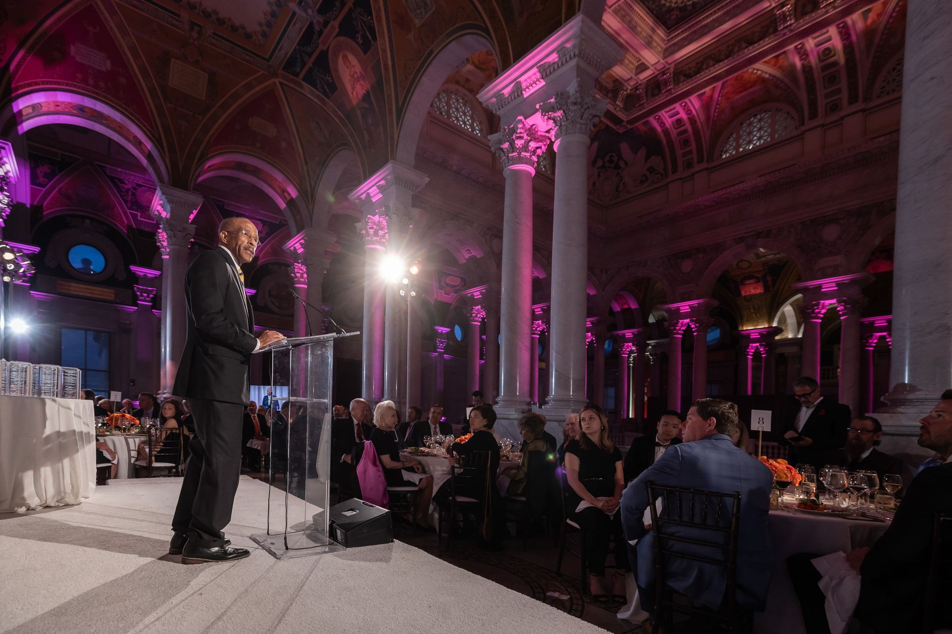 A man is giving a speech at a podium in a large room.