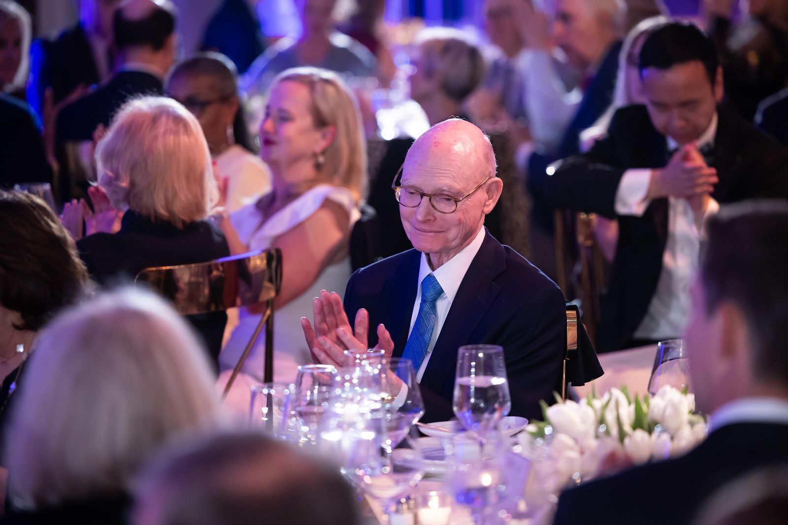 A man in a suit and tie is sitting at a table with glasses of water.
