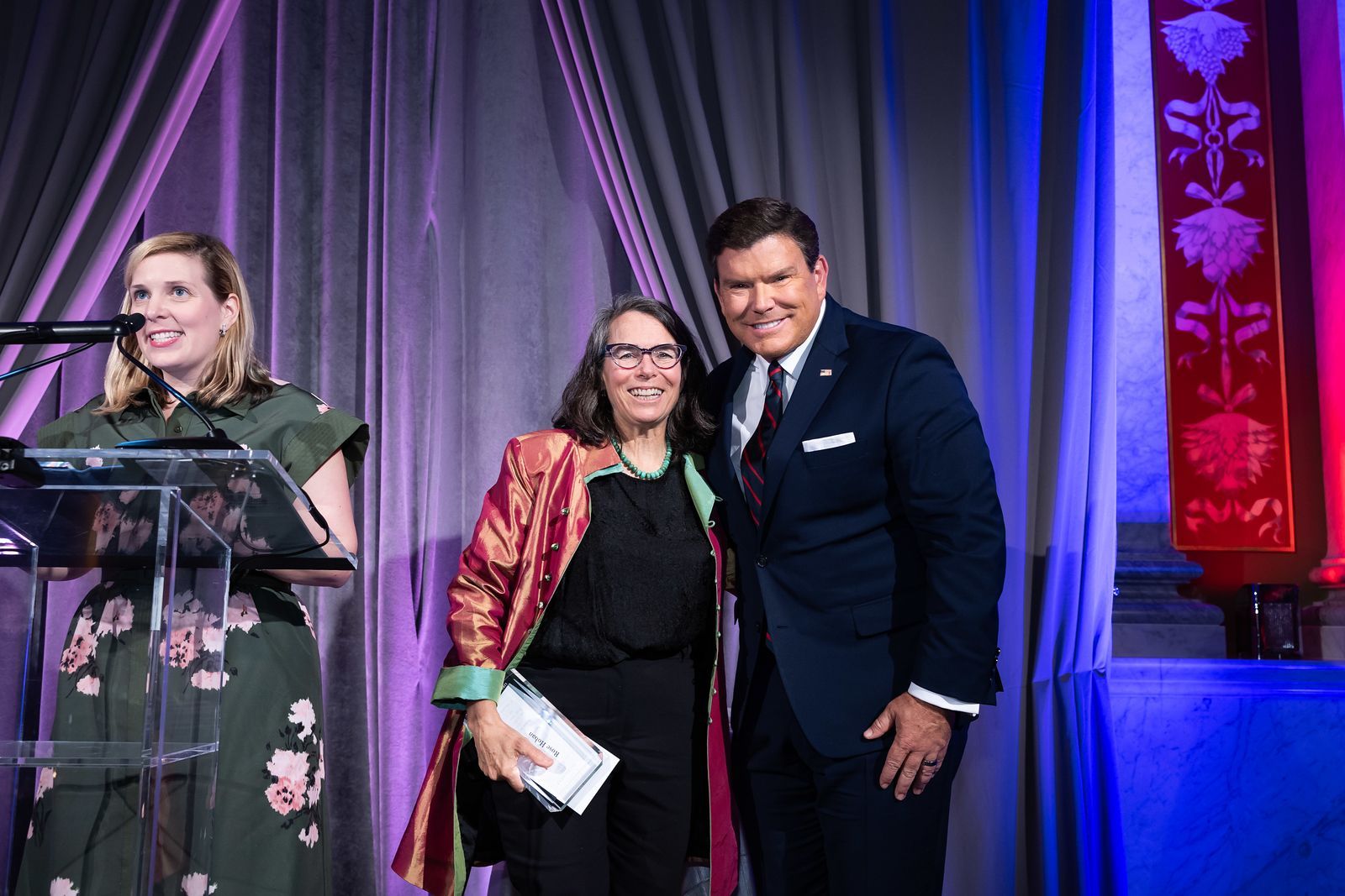 A woman is giving a speech at a podium next to a man and a woman.