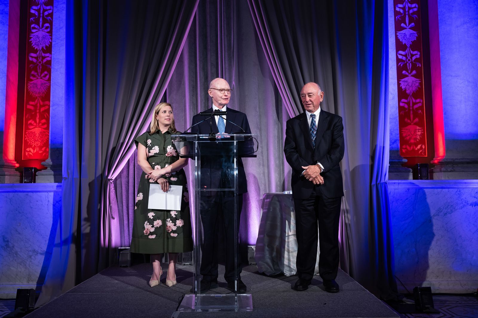 Three people are standing at a podium giving a speech.