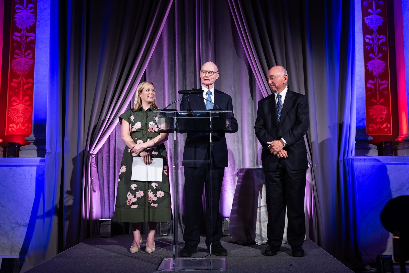 A man is standing at a podium giving a speech while two other people stand behind him.