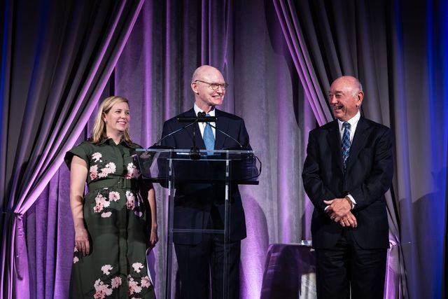 A man in a suit is standing at a podium with two other people.