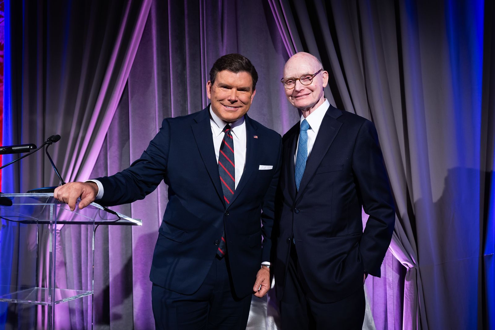 Two men in suits and ties are standing next to each other in front of a podium.