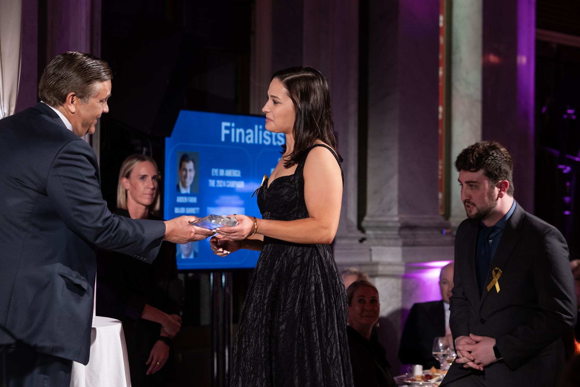 A man is giving an award to a woman in a black dress.