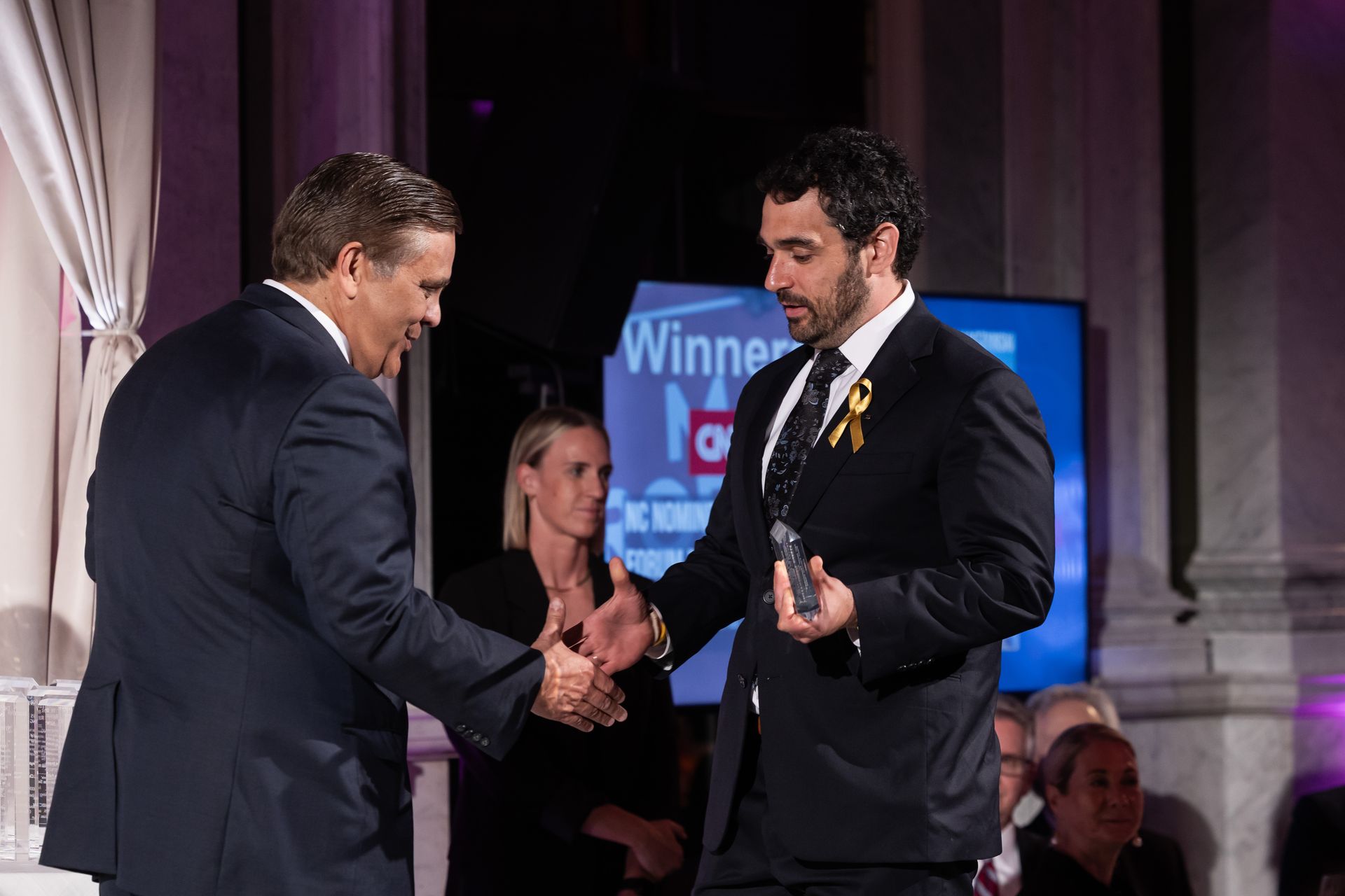 A man in a suit is shaking hands with another man while holding an award.