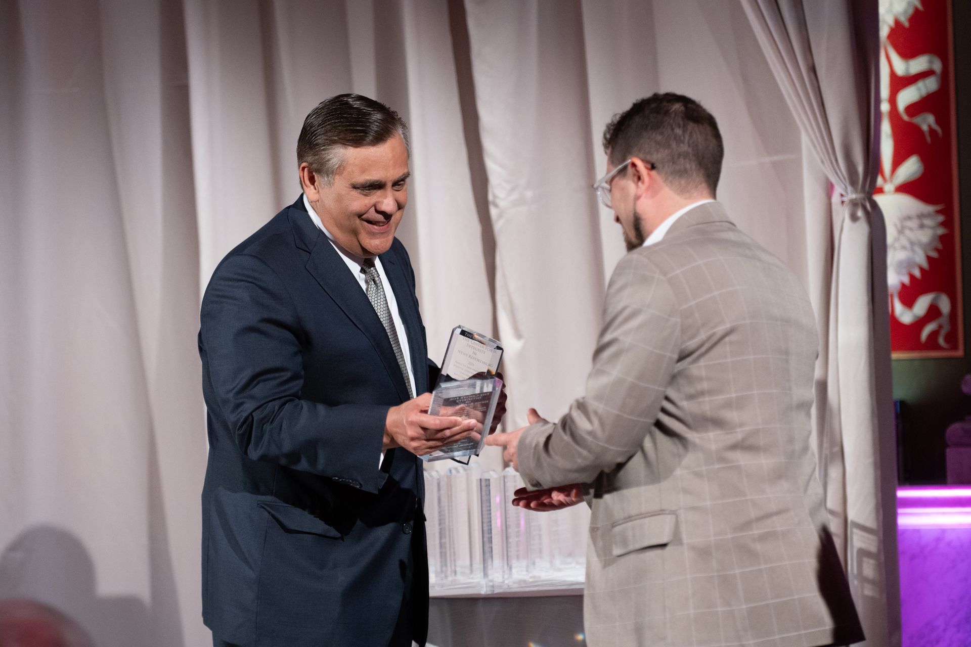A man in a suit is giving an award to another man in a suit.