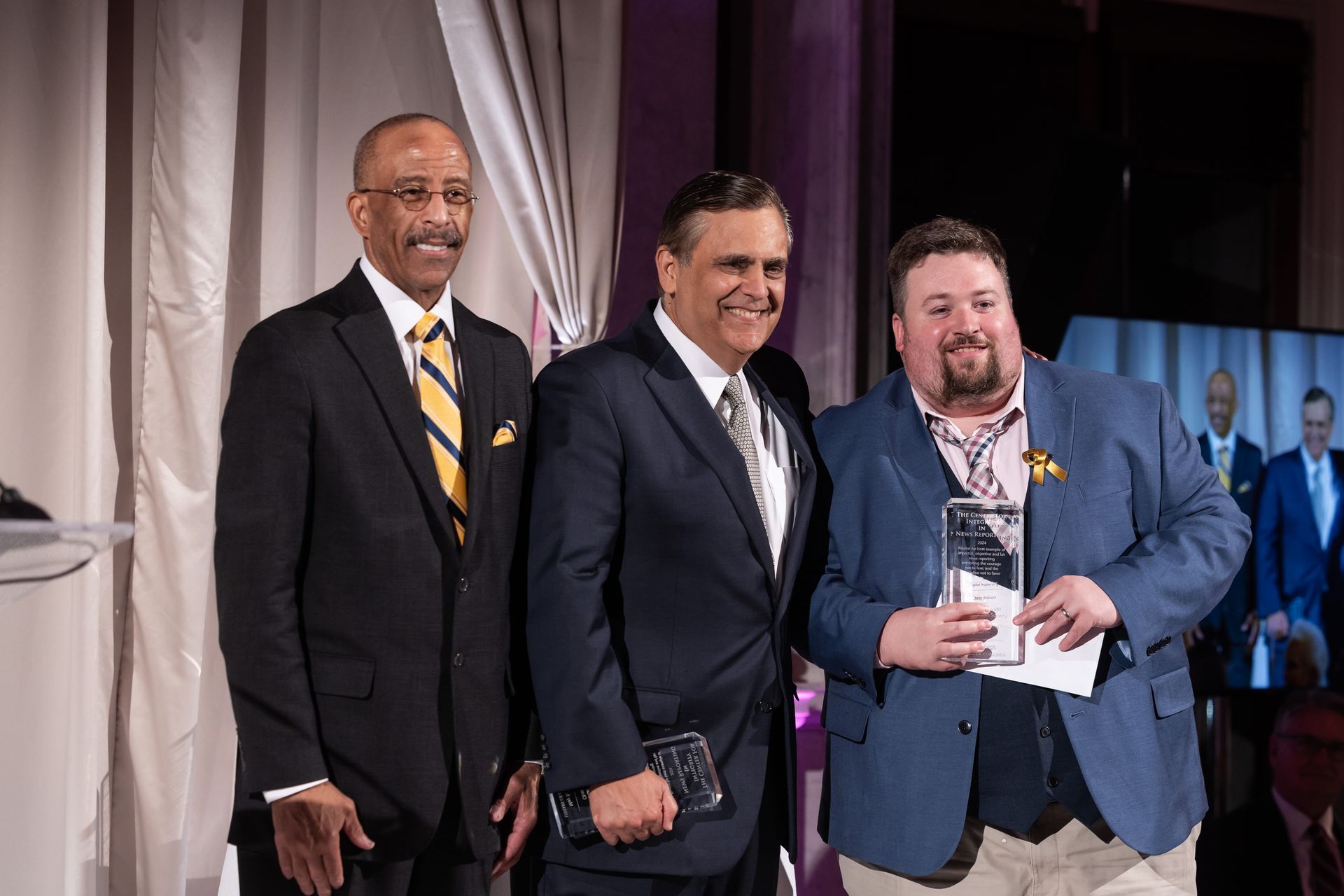 Three men in suits and ties are standing next to each other on a stage.