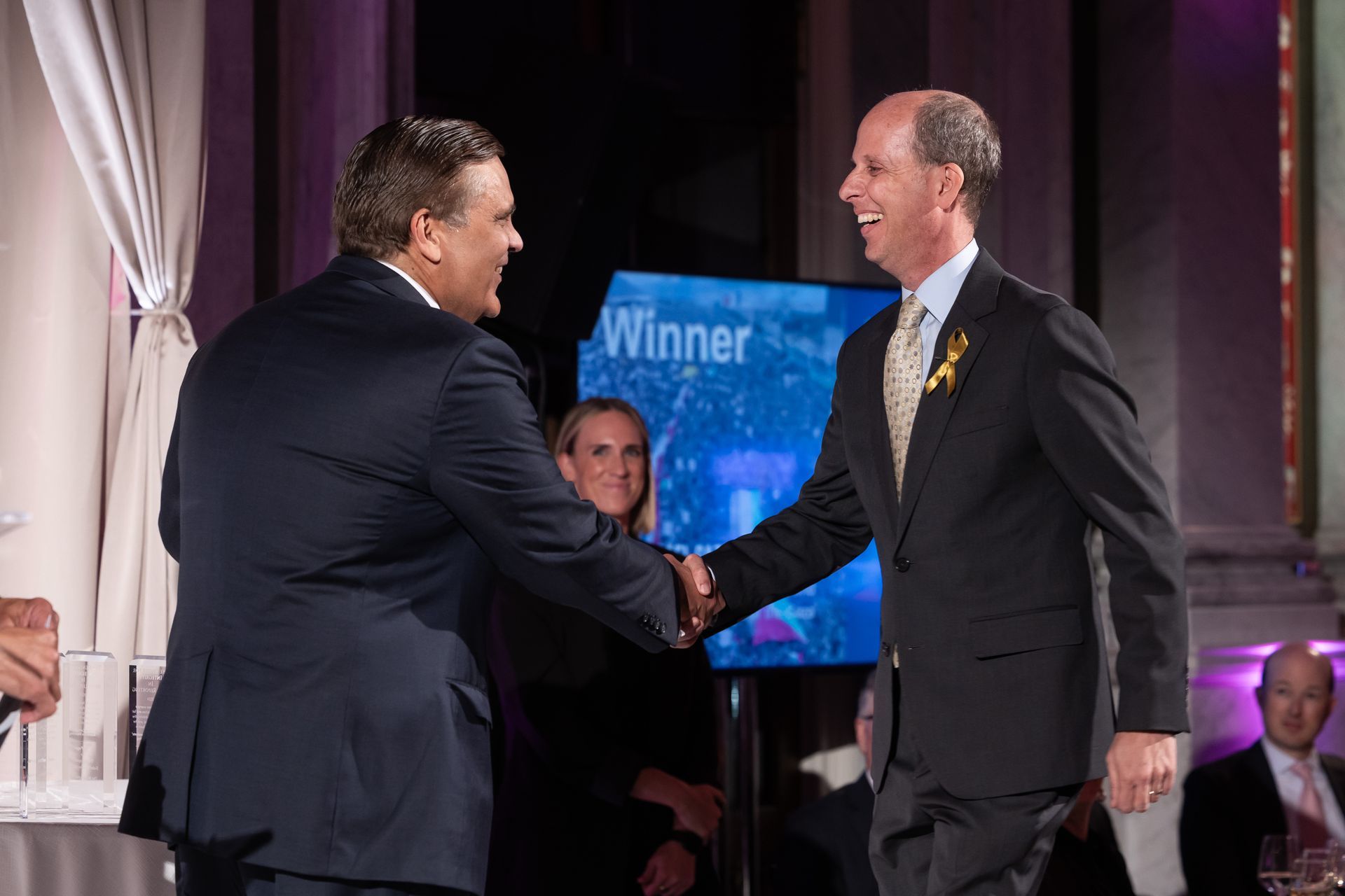 Two men shaking hands in front of a screen that says winner