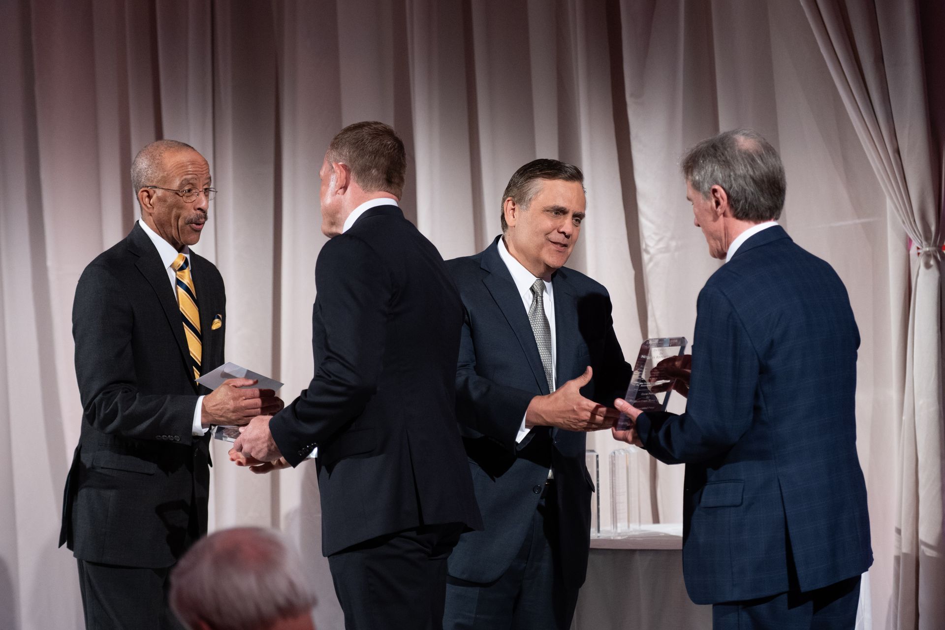 A group of men in suits are shaking hands on a stage.