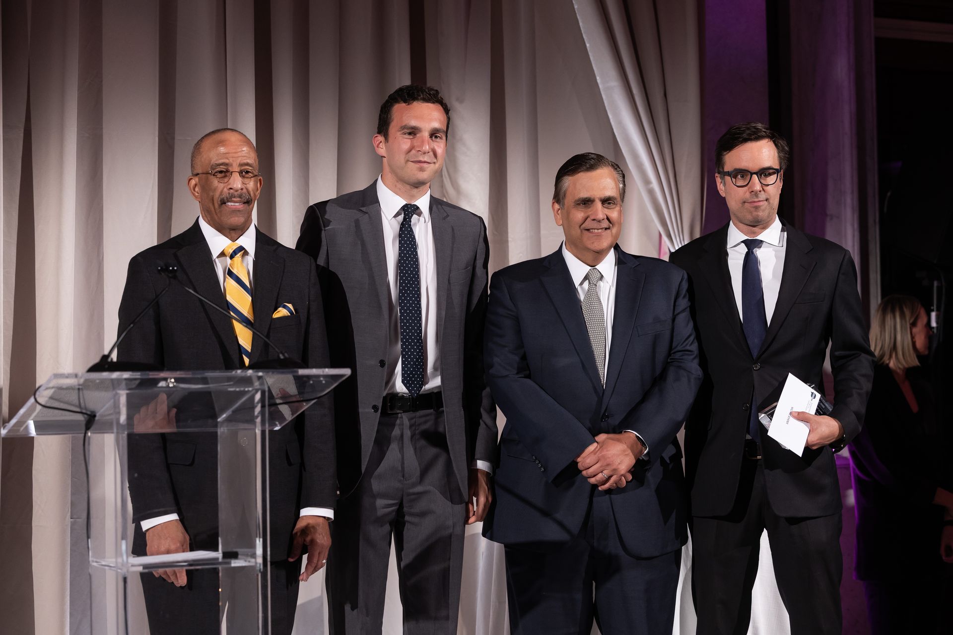 Four men in suits and ties are standing in front of a podium.
