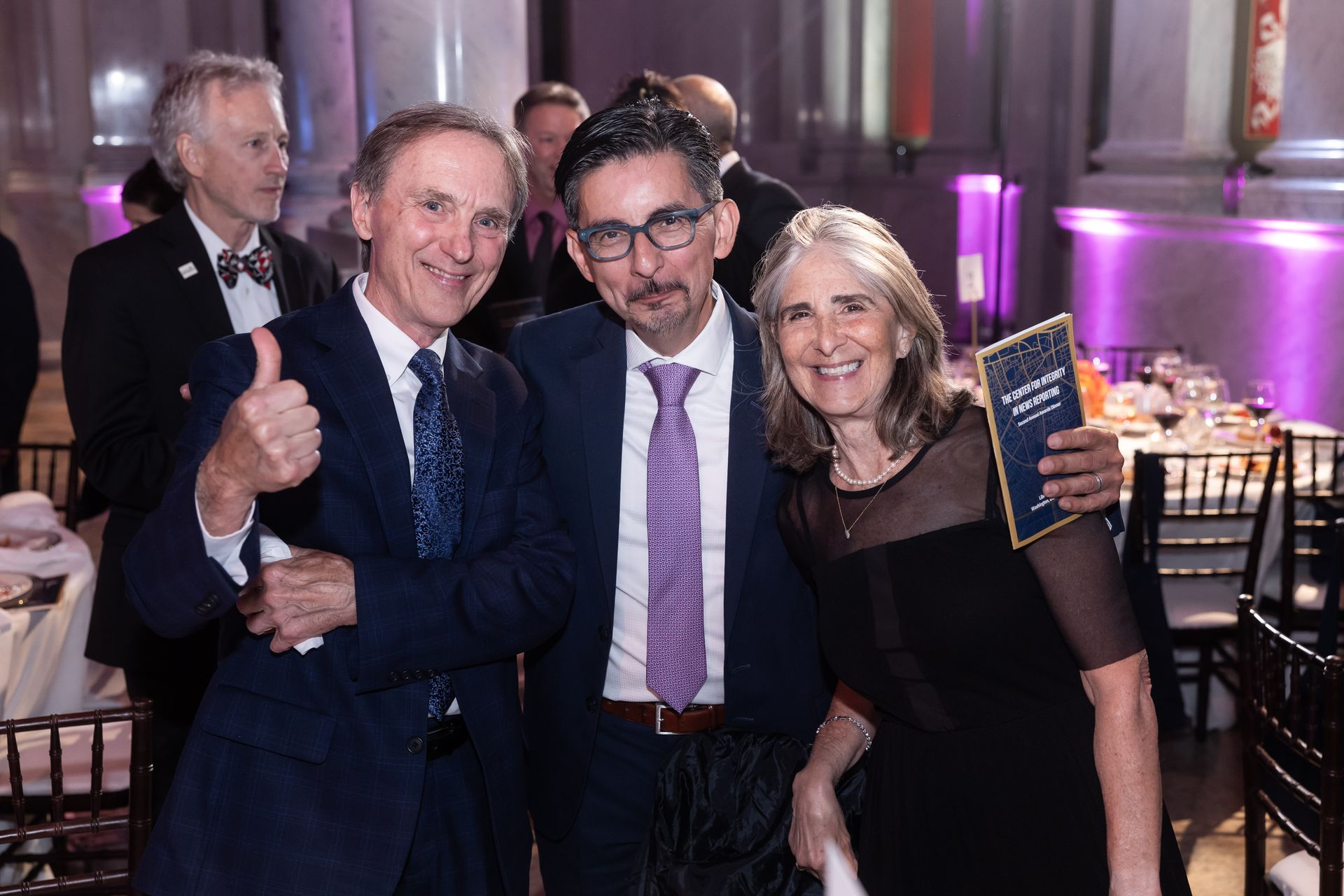 Three people are posing for a picture at a party and one of them is giving a thumbs up.