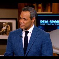 A man in a suit and tie is standing in front of a television.