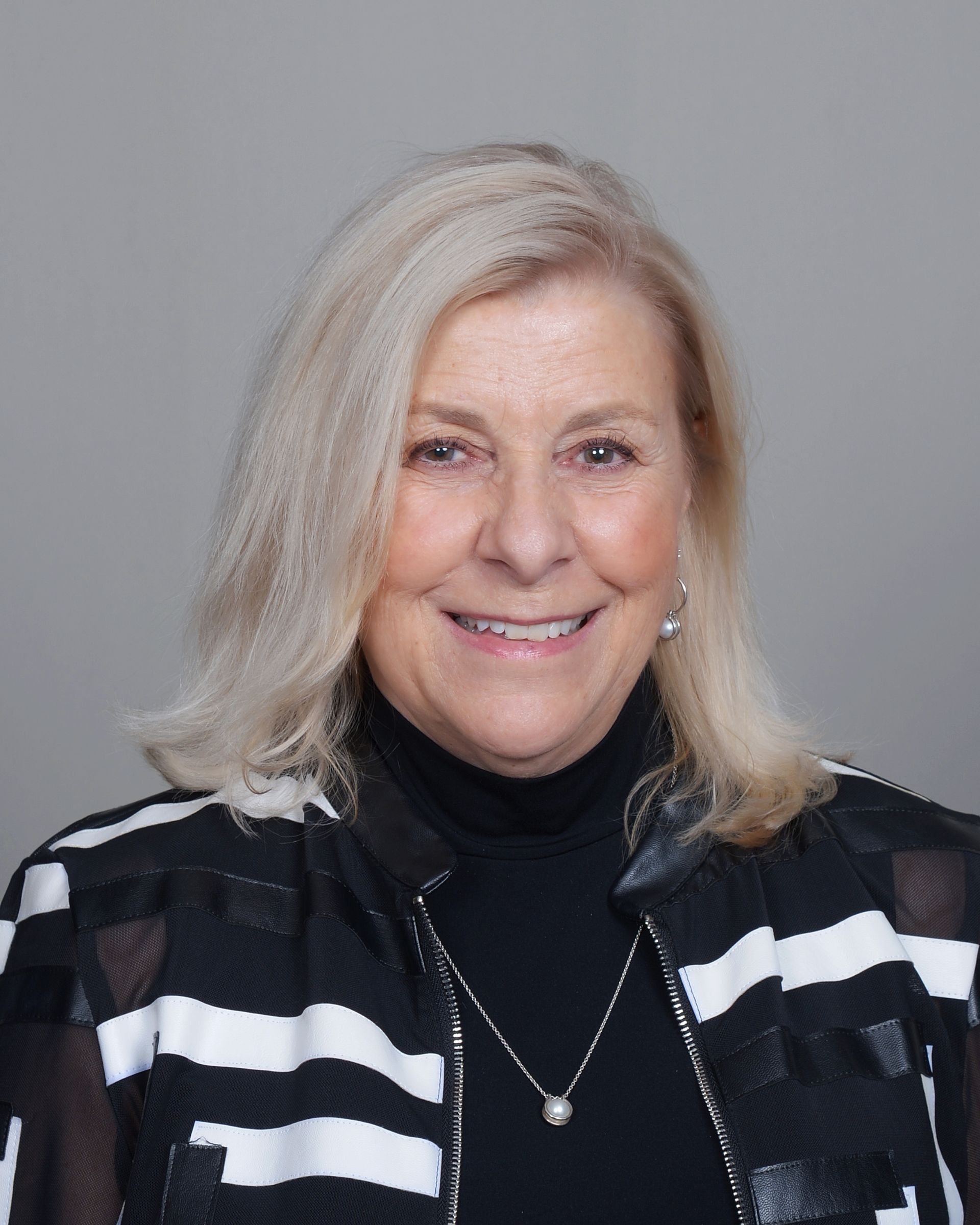 A woman wearing a black and white jacket and a necklace is smiling for the camera.