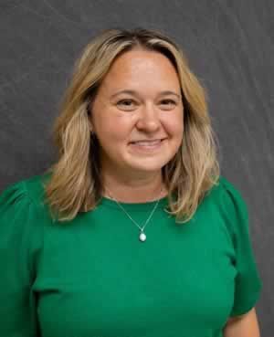 A woman in a green shirt and necklace is smiling for the camera.