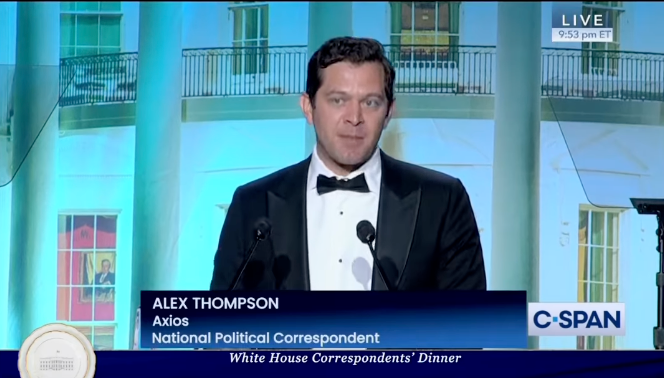 A man in a tuxedo is giving a speech in front of a microphone