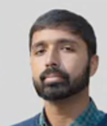 A man with a beard is wearing a blue sweater and a plaid shirt.