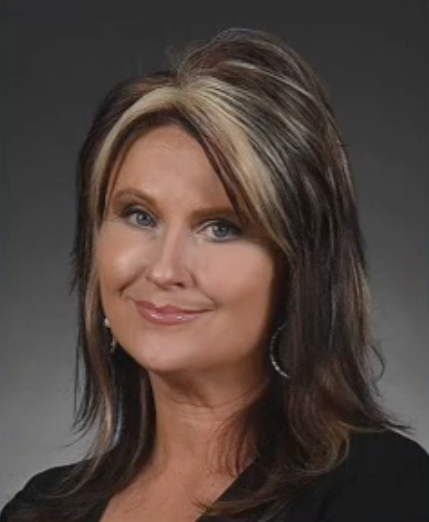 A woman with long brown hair and blonde highlights is smiling for the camera.