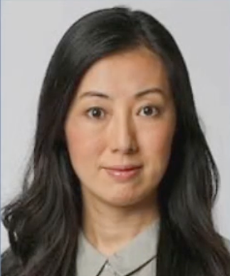A woman with long black hair is wearing a grey shirt and tie.