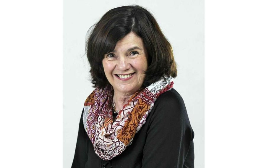 Woman smiling, wearing a patterned scarf and black top, against a white background.