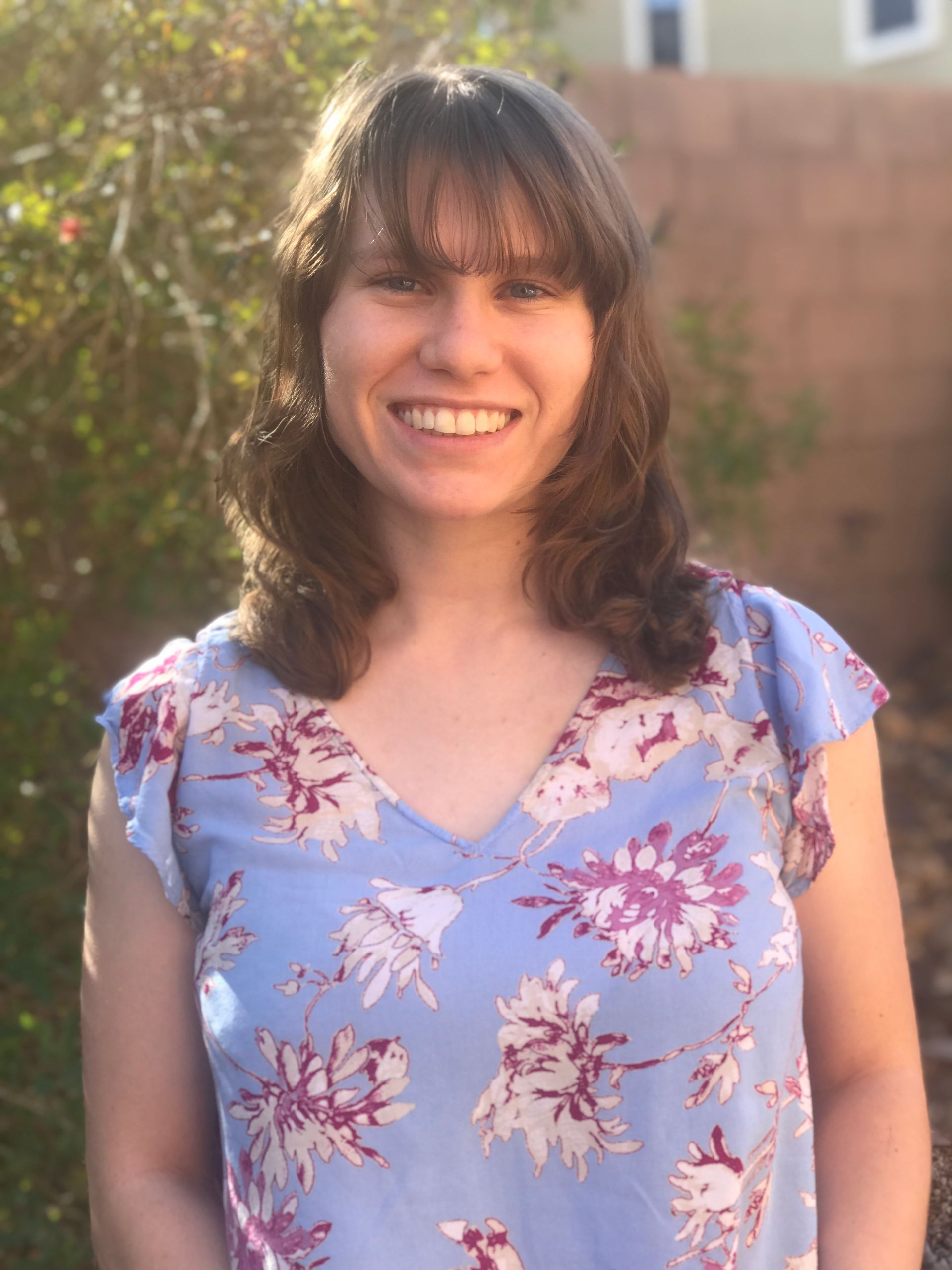 A woman in a blue floral shirt is smiling for the camera.