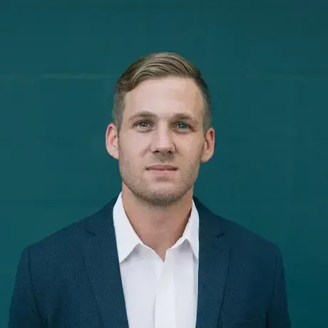 A man in a suit and white shirt is standing in front of a blue wall.