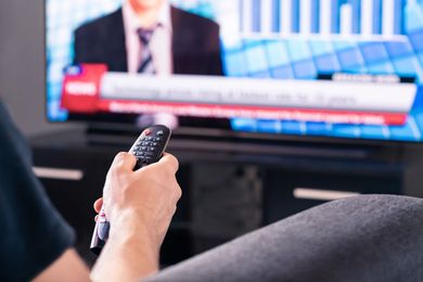 A person is holding a remote control in front of a television.