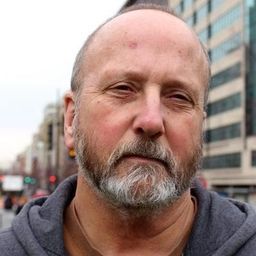 A bald man with a beard and mustache is standing in front of a building.